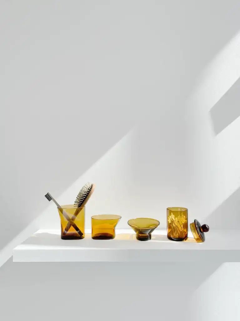 Cala collection of mouth blown glass toothbrush and other bathroom product holders and Mika a small container in the color amber.