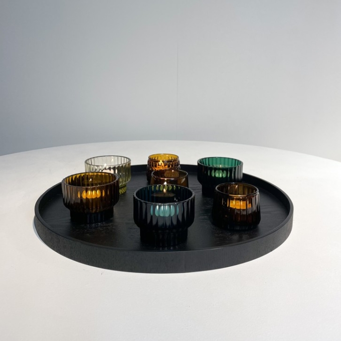 Collection of XLBoom Serve trays in sleek black finish, displayed in various shapes and sizes—round, rectangular, and square—on a smooth concrete floor. Each tray features a subtle wood grain texture and raised edges, showcasing the minimalist design and versatility of the Serve series.